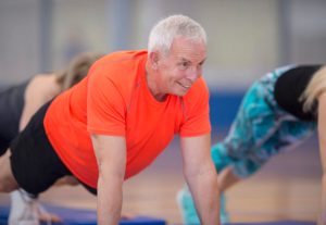 A group of adults are taking a fitness class together at the gym. They are working out on exercise mats and are holding a high plank.